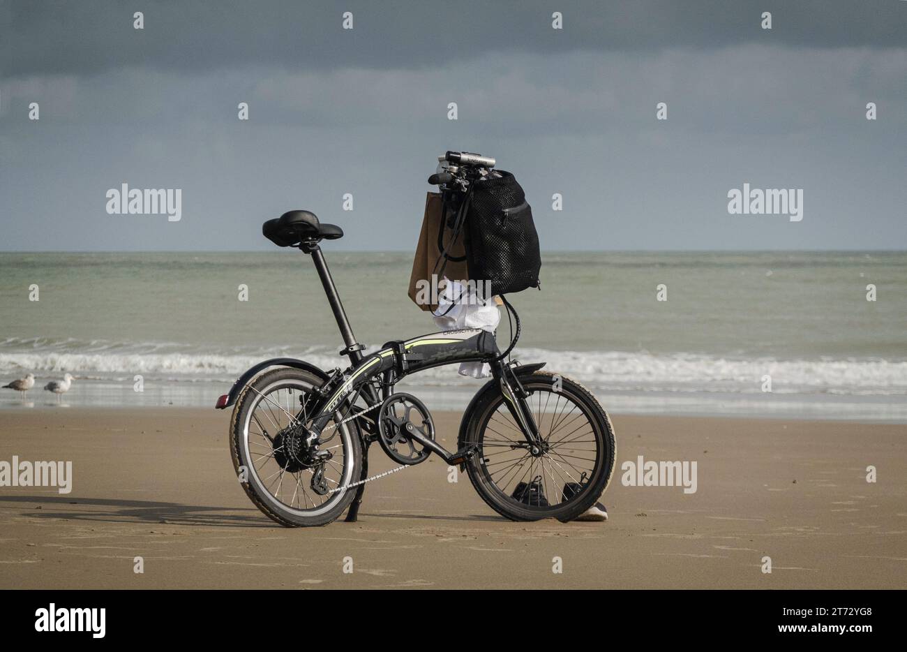 Vélo équilibré sur un stand, sur une plage de sable vide, avec deux mouettes et une paire de baskets. Carrero Crosscity E. Banque D'Images