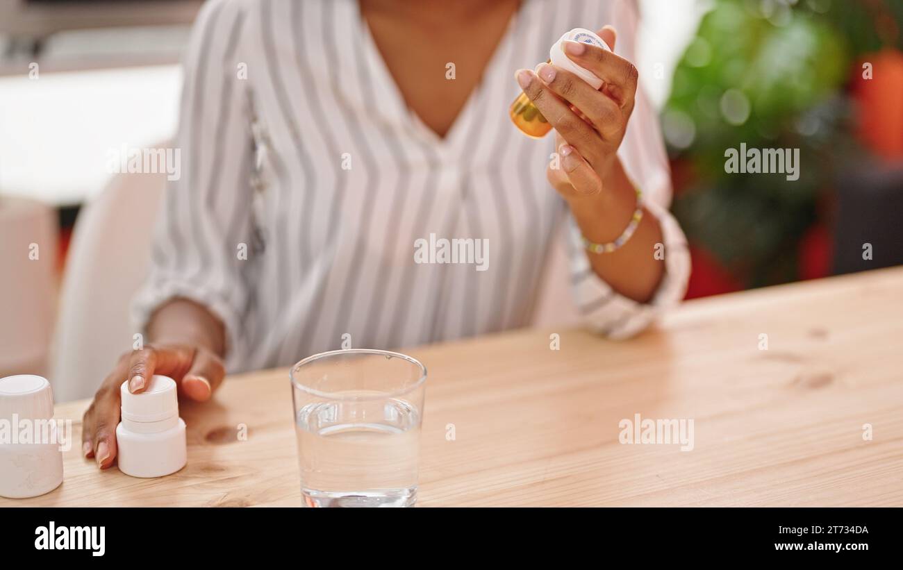 Femme afro-américaine tenant des bouteilles de pilules dans la salle à manger Banque D'Images