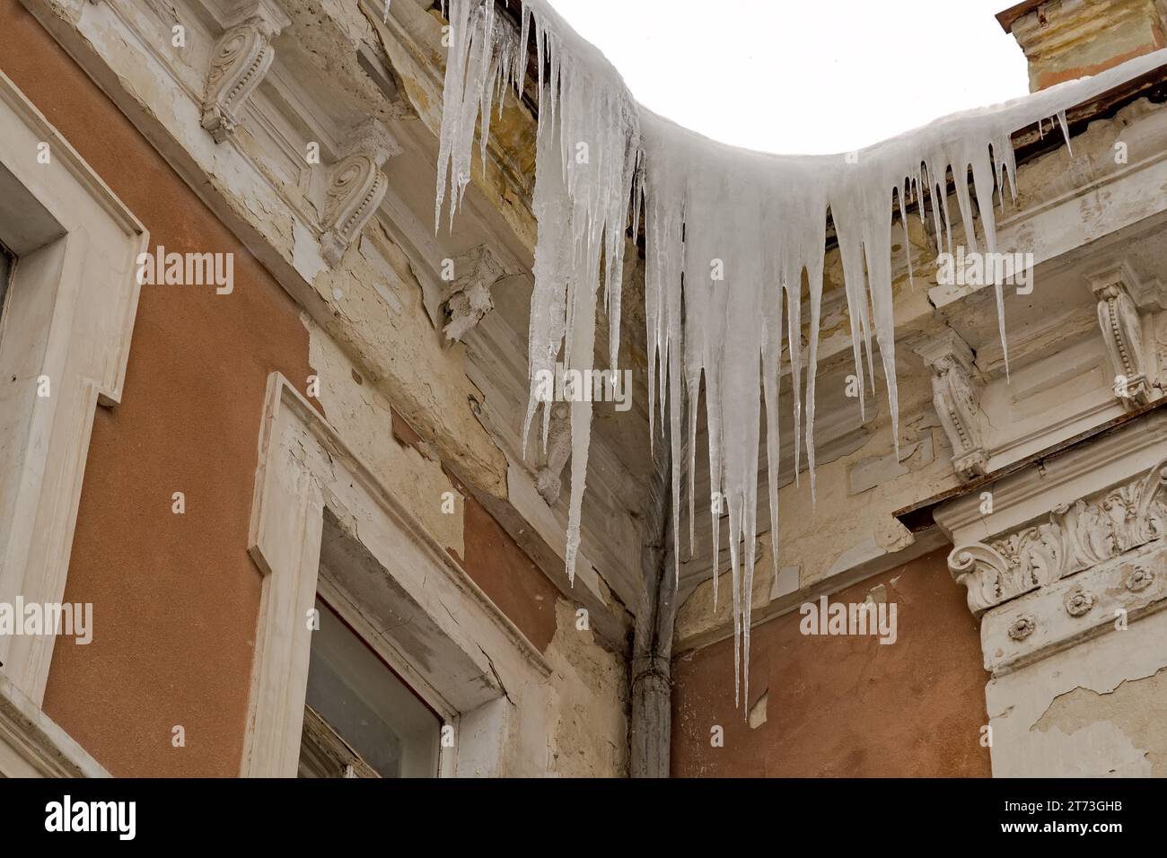 D'énormes glaçons pendent de l'avant-toit d'un vieux bâtiment, menaçant de tomber. Banque D'Images