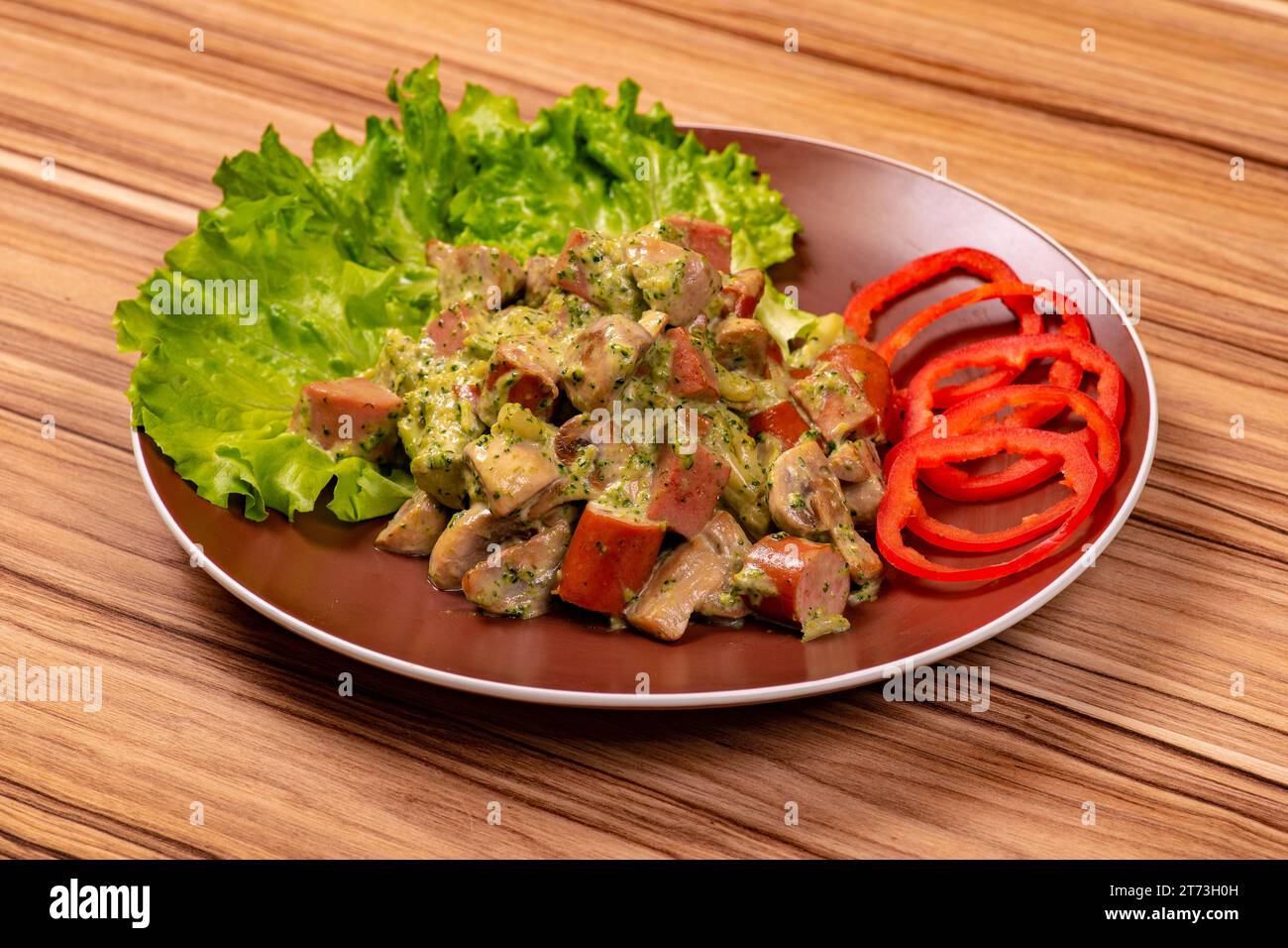 Salade avec saucisse tranchée en sauce blanche avec des rondelles de poivron sur une assiette sur une table en bois Banque D'Images