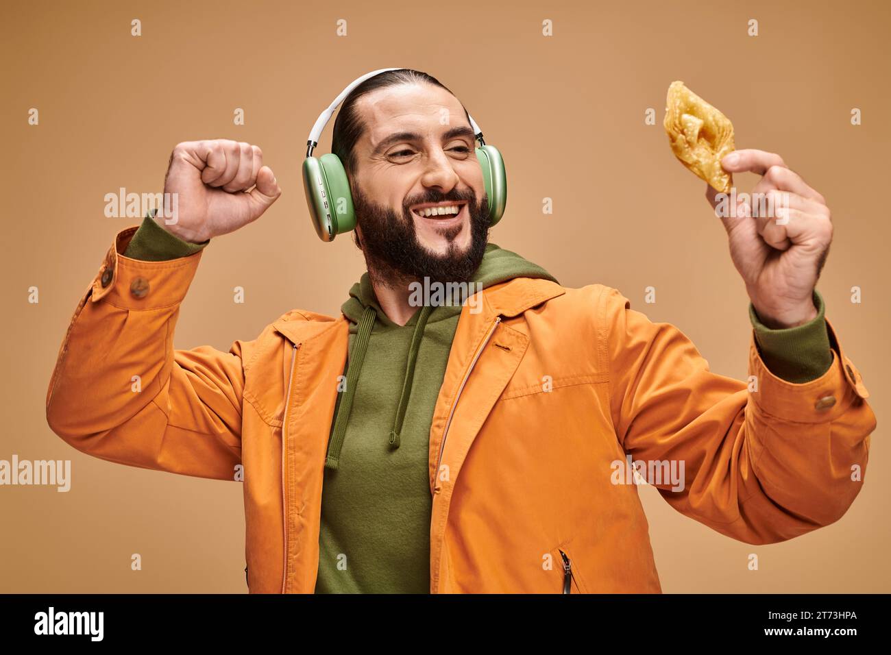 heureux homme arabe dans les écouteurs tenant baklava miel sur fond beige, dessert moyen-oriental Banque D'Images