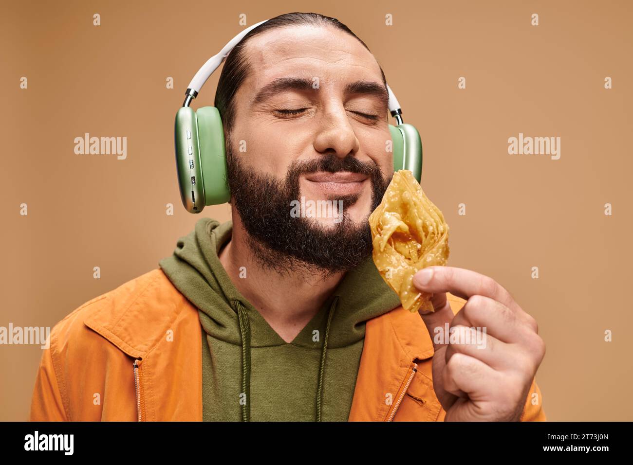 homme arabe heureux dans les écouteurs sentant baklava miel sur fond beige, dessert moyen-oriental Banque D'Images