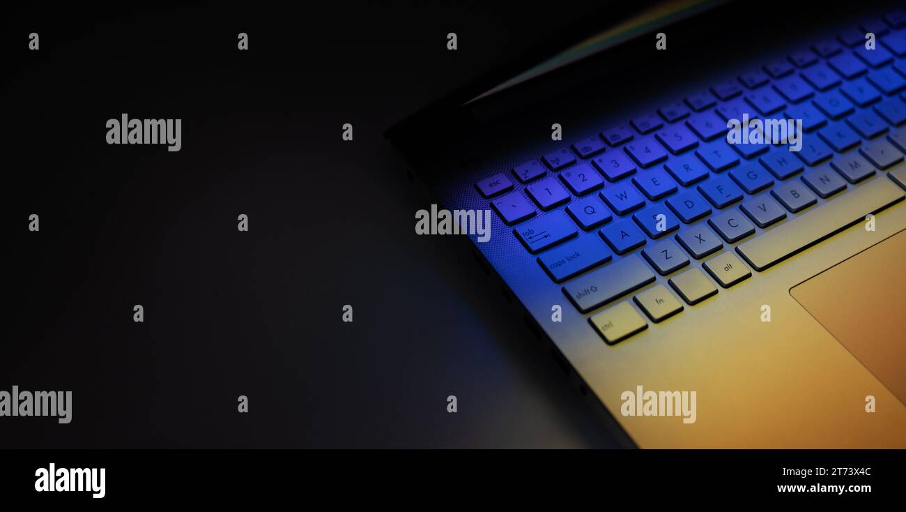 gros plan du clavier d'ordinateur portable sur la table sombre avec réflexion lumineuse colorée. bannière avec espace de copie Banque D'Images
