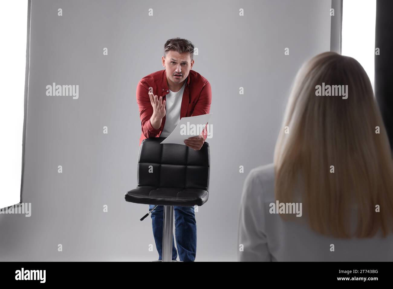 Homme avec script se produisant devant le directeur de casting sur fond gris clair en studio Banque D'Images