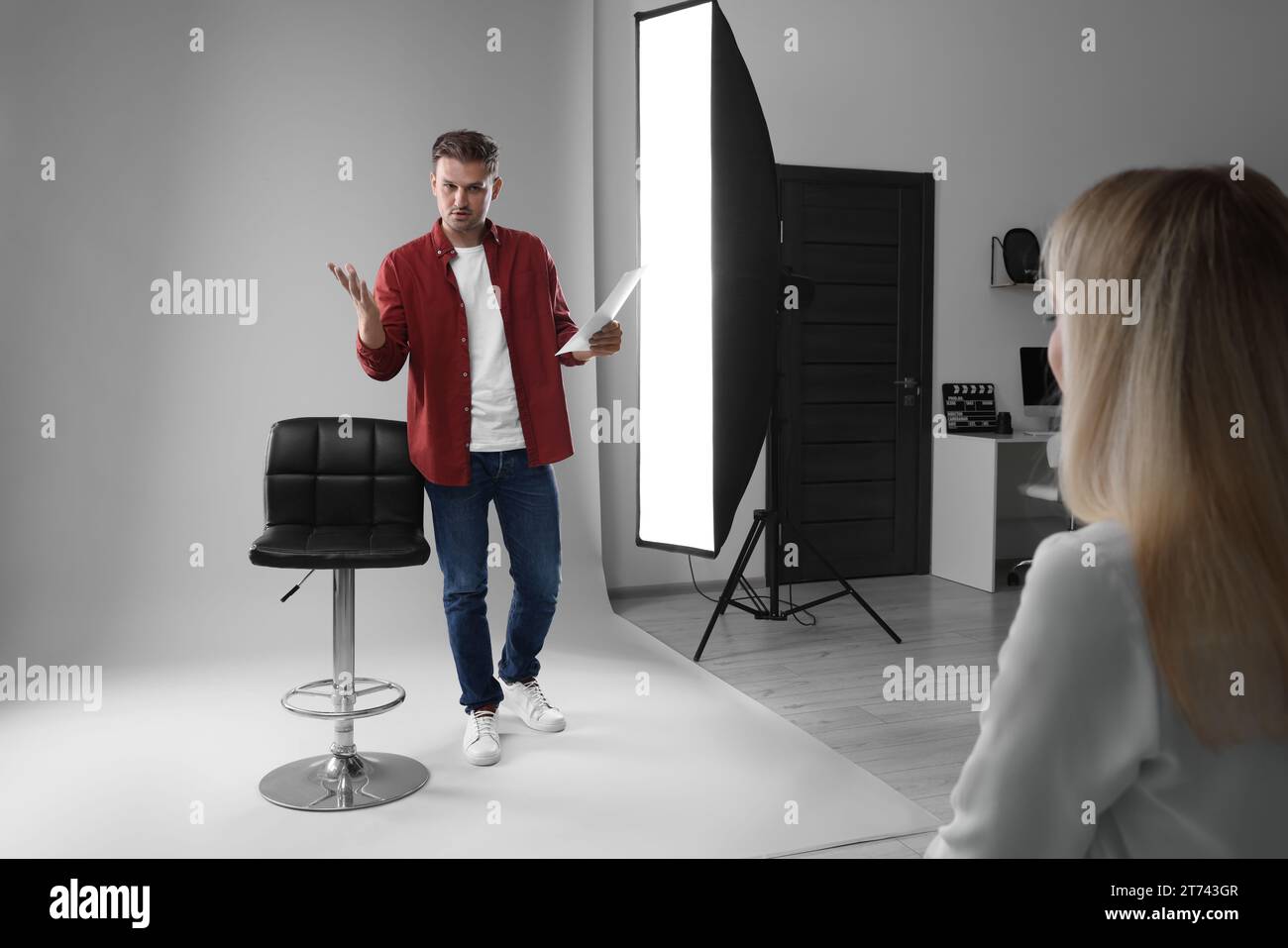 Homme avec script se produisant devant le directeur de casting sur fond gris clair en studio Banque D'Images