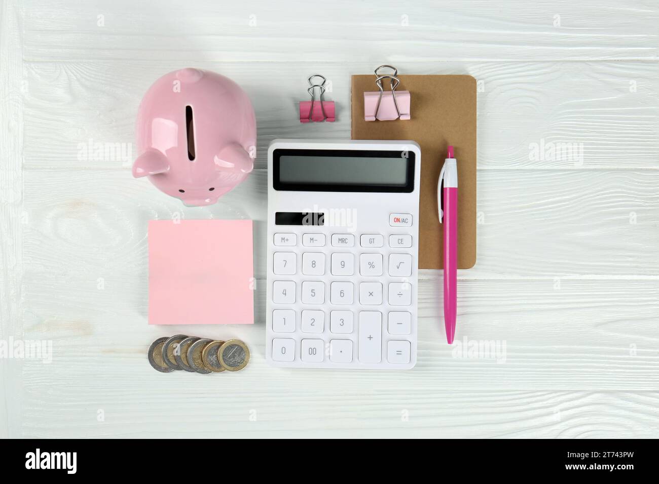 Calculatrice, pièces de monnaie, tirelire, cahier, pinces à reliure et stylo sur table en bois blanc, pose à plat. Concept de retraite Banque D'Images