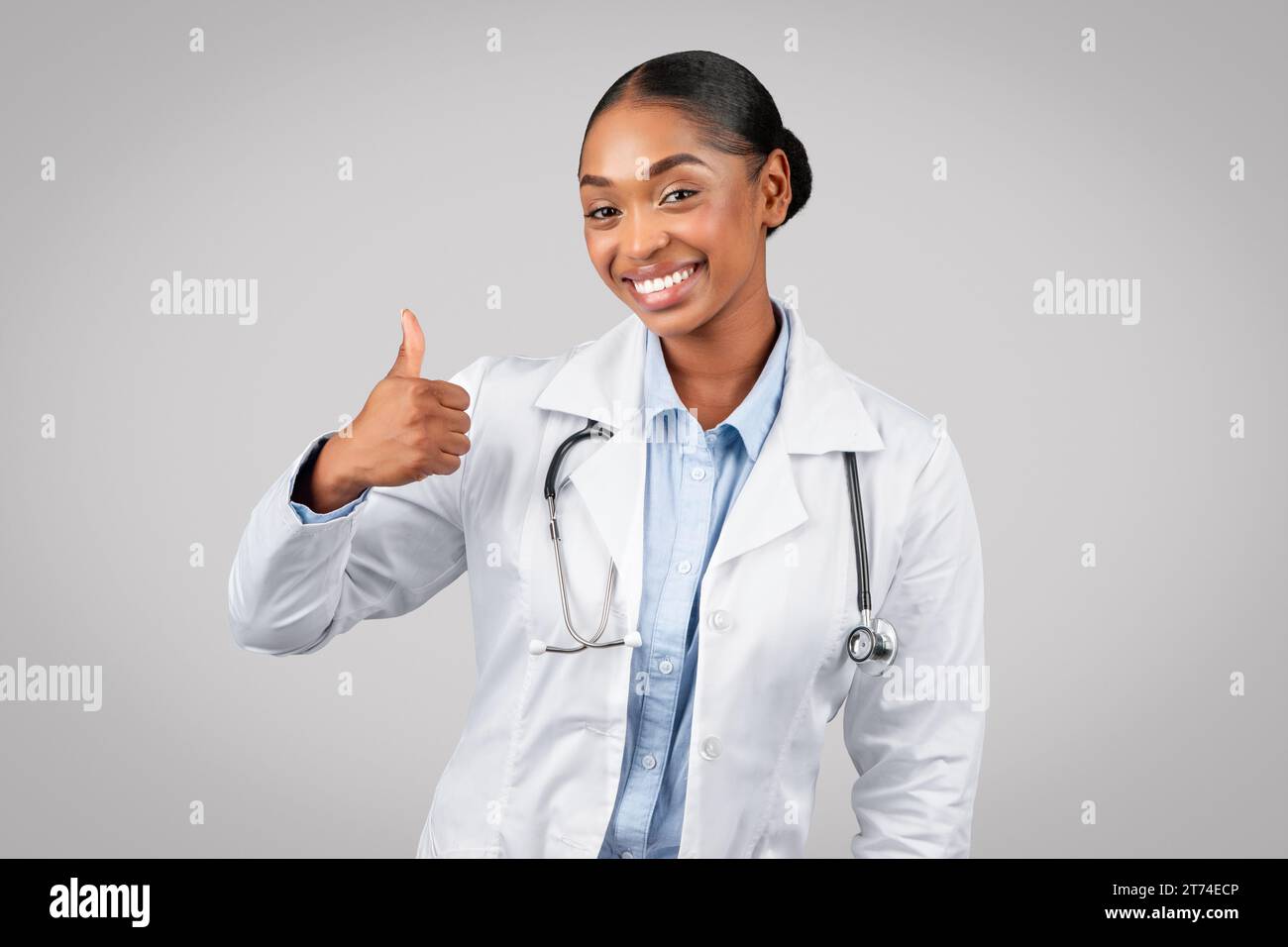Joyeux joli millennial dame noire docteur en manteau blanc faire le pouce vers le haut signe avec la main Banque D'Images
