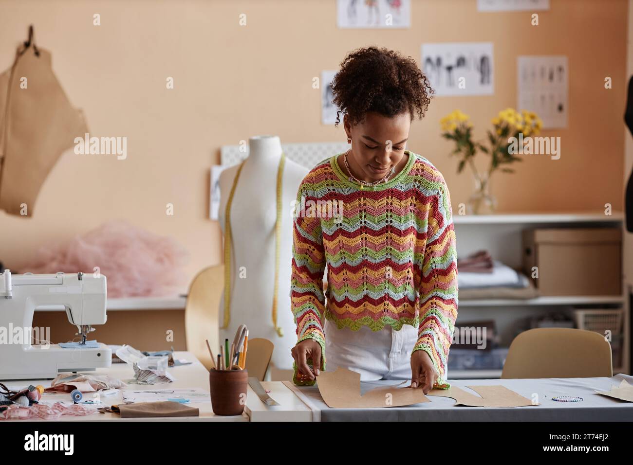 Jeune artisan créatif se penchant sur la table avec des patrons de couture et du textile tout en travaillant sur de nouveaux vêtements dans son atelier Banque D'Images