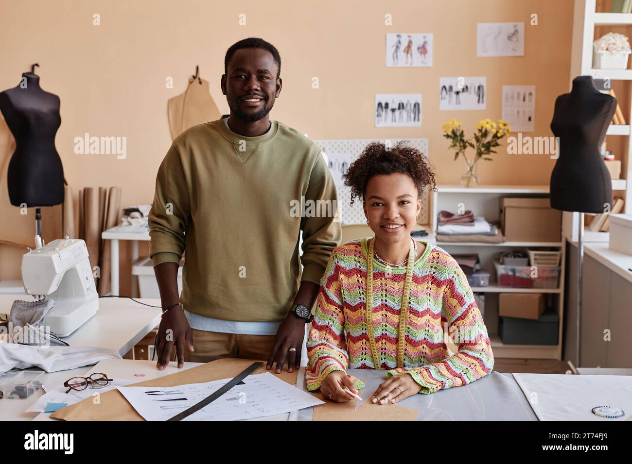 Deux jeunes créateurs de mode afro-américains regardant la caméra avec des sourires tandis que la femme tailleur contournant des patrons de papier à coudre Banque D'Images