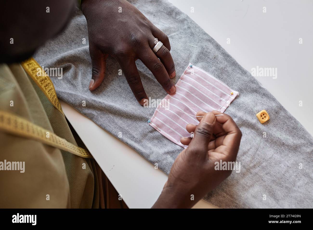 Au-dessus de l'angle des mains du styliste masculin afro-américain cousant un petit patch sur un pantalon tout en personnalisant de vieux vêtements par table en atelier Banque D'Images