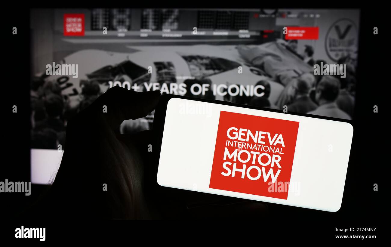 Personne tenant le téléphone portable avec le logo du salon suisse de l'auto Genève International Motor Show en face de la page Web de l'entreprise. Concentrez-vous sur l'affichage du téléphone. Banque D'Images