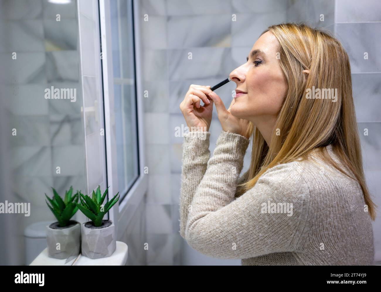 femme appliquant du maquillage (peindre ses cils) pour un rendez-vous du soir devant un miroir. Banque D'Images