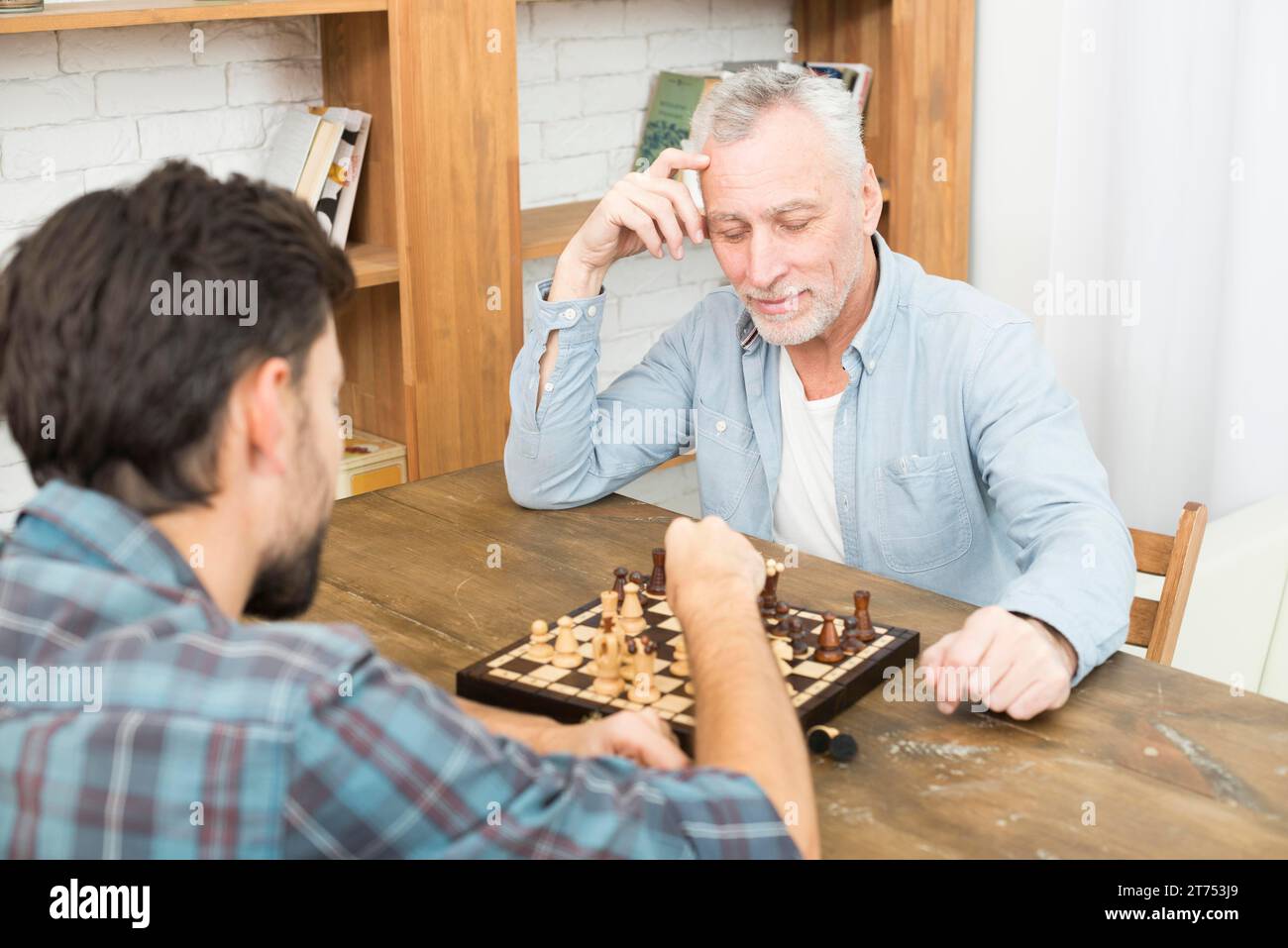 Pensif homme âgé jeune gars jouant à la table d'échecs près des étagères Banque D'Images