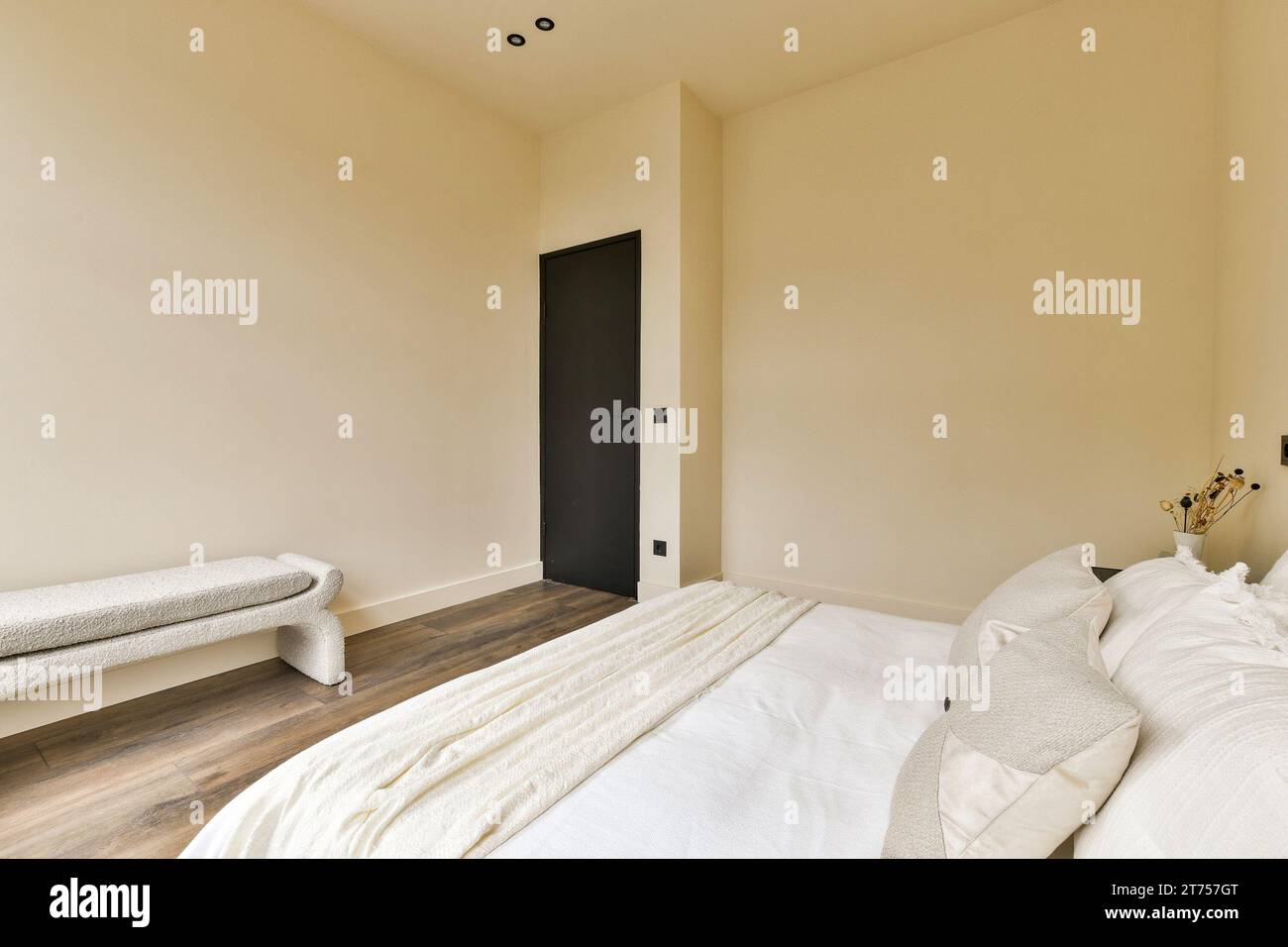 une chambre avec parquet et draps blancs sur le lit, il y a une porte noire dans la chambre Banque D'Images