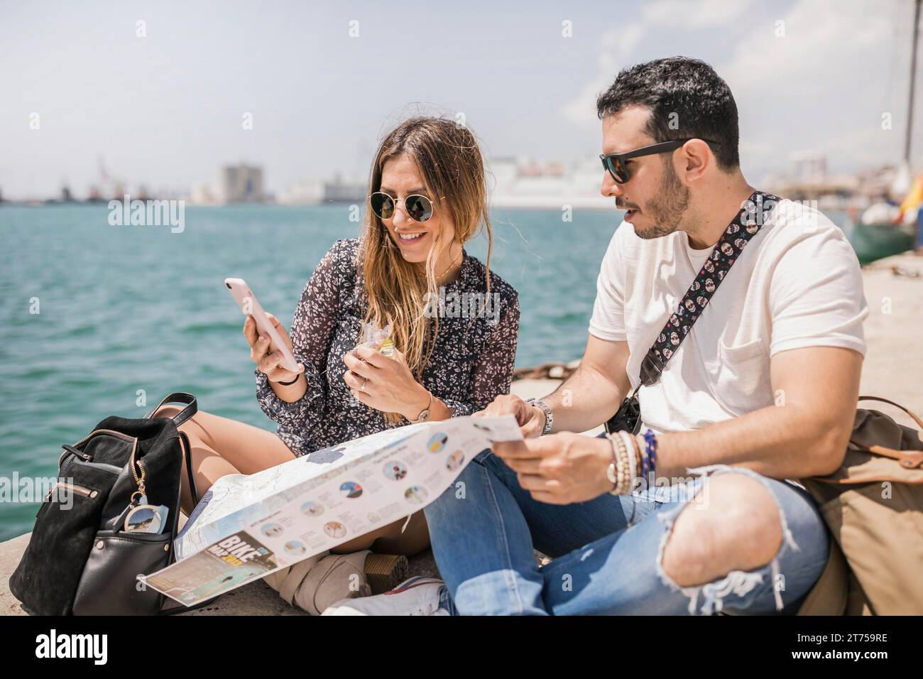 Touriste femme montrant son petit ami téléphone portable assis jetée Banque D'Images
