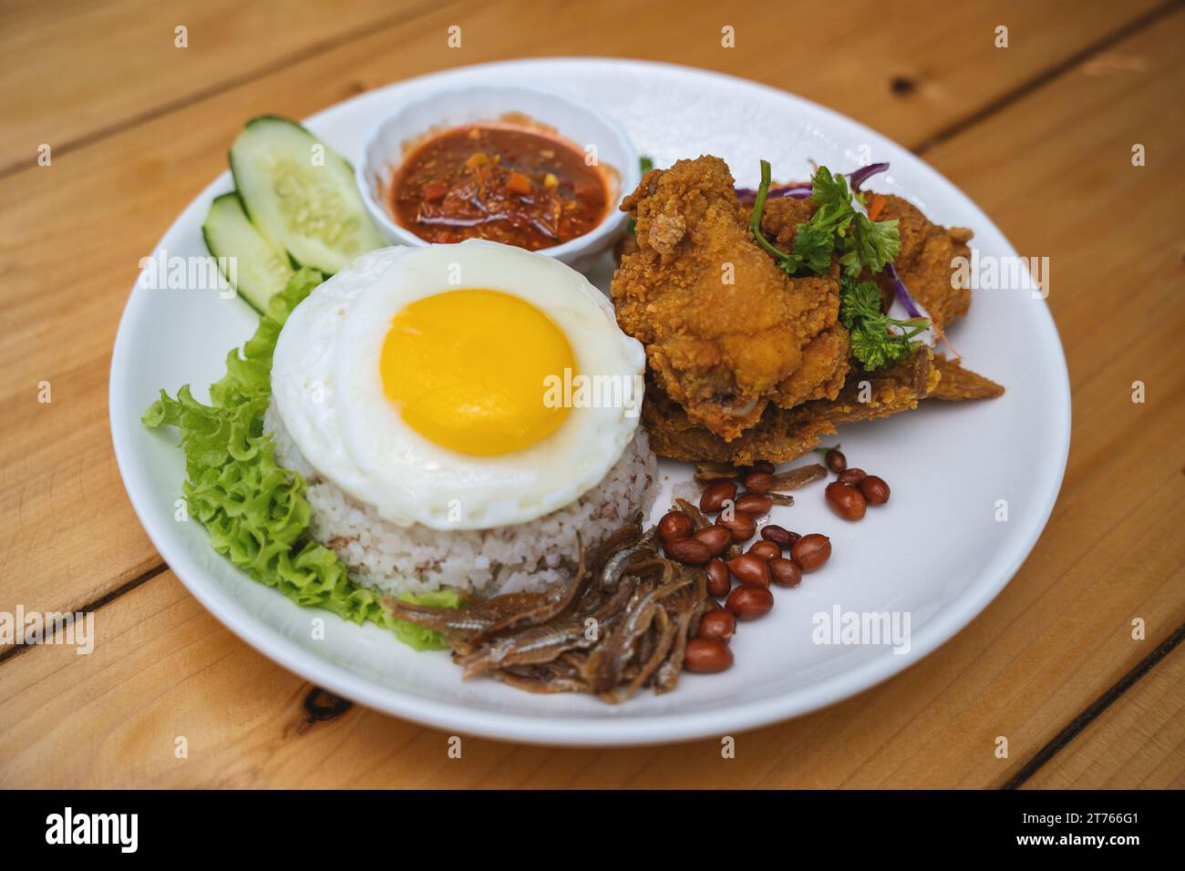 Nasi Lemak avec poulet frit et œuf sur une assiette blanche avec concombre Banque D'Images