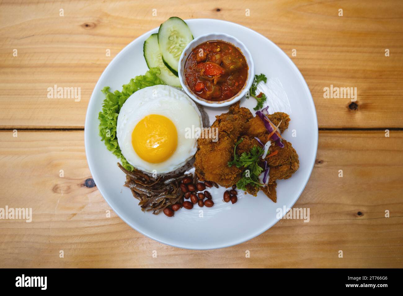 Nasi Lemak avec poulet frit et œuf sur une assiette blanche avec concombre Banque D'Images