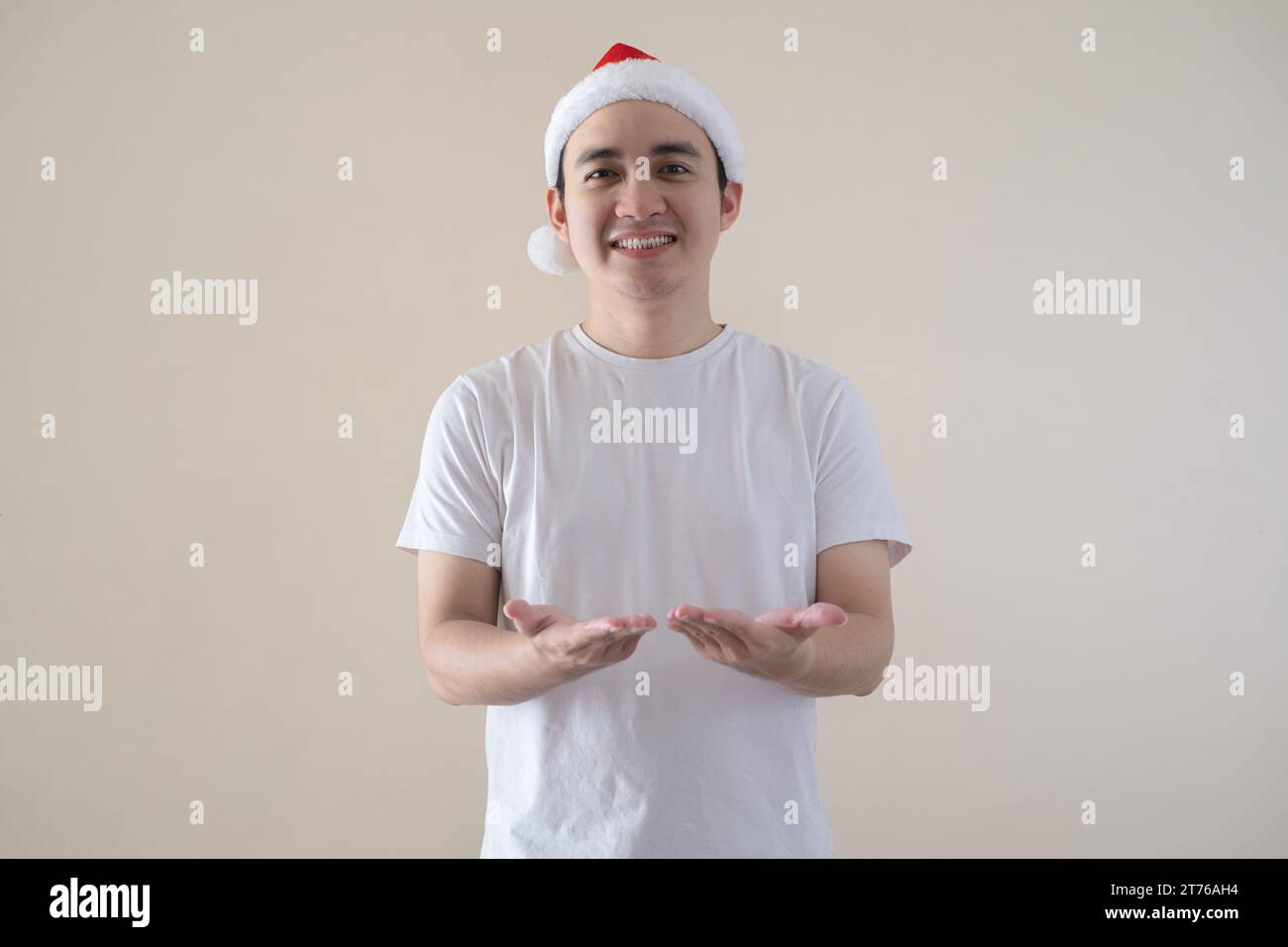 Jeune père Noël asiatique ouvre ses paumes à la caméra avec l'expression du visage de sourire sur fond beige isolé. Concept de Noël. Banque D'Images