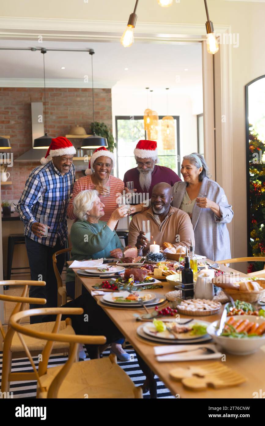 Heureux groupe diversifié d'amis seniors dans les chapeaux de père noël célébrant avec le repas de noël et le grillage Banque D'Images