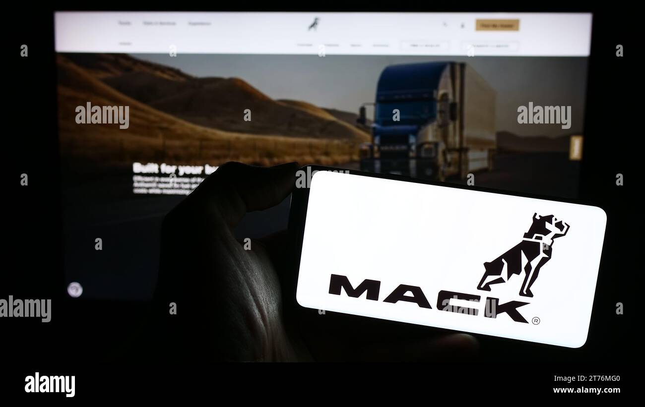 Personne tenant le téléphone portable avec le logo de la société américaine de fabrication de camions Mack Trucks Inc. En face de la page Web d'affaires. Concentrez-vous sur l'affichage du téléphone. Banque D'Images