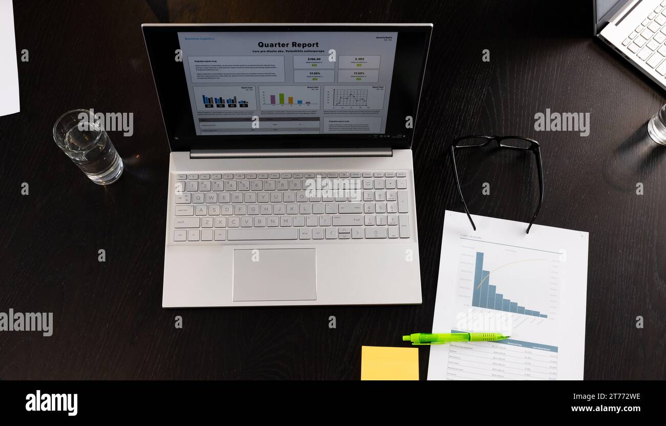 Ordinateur portable avec texte et graphiques de rapport de trimestre à l'écran et document sur table dans la salle de réunion de bureau Banque D'Images