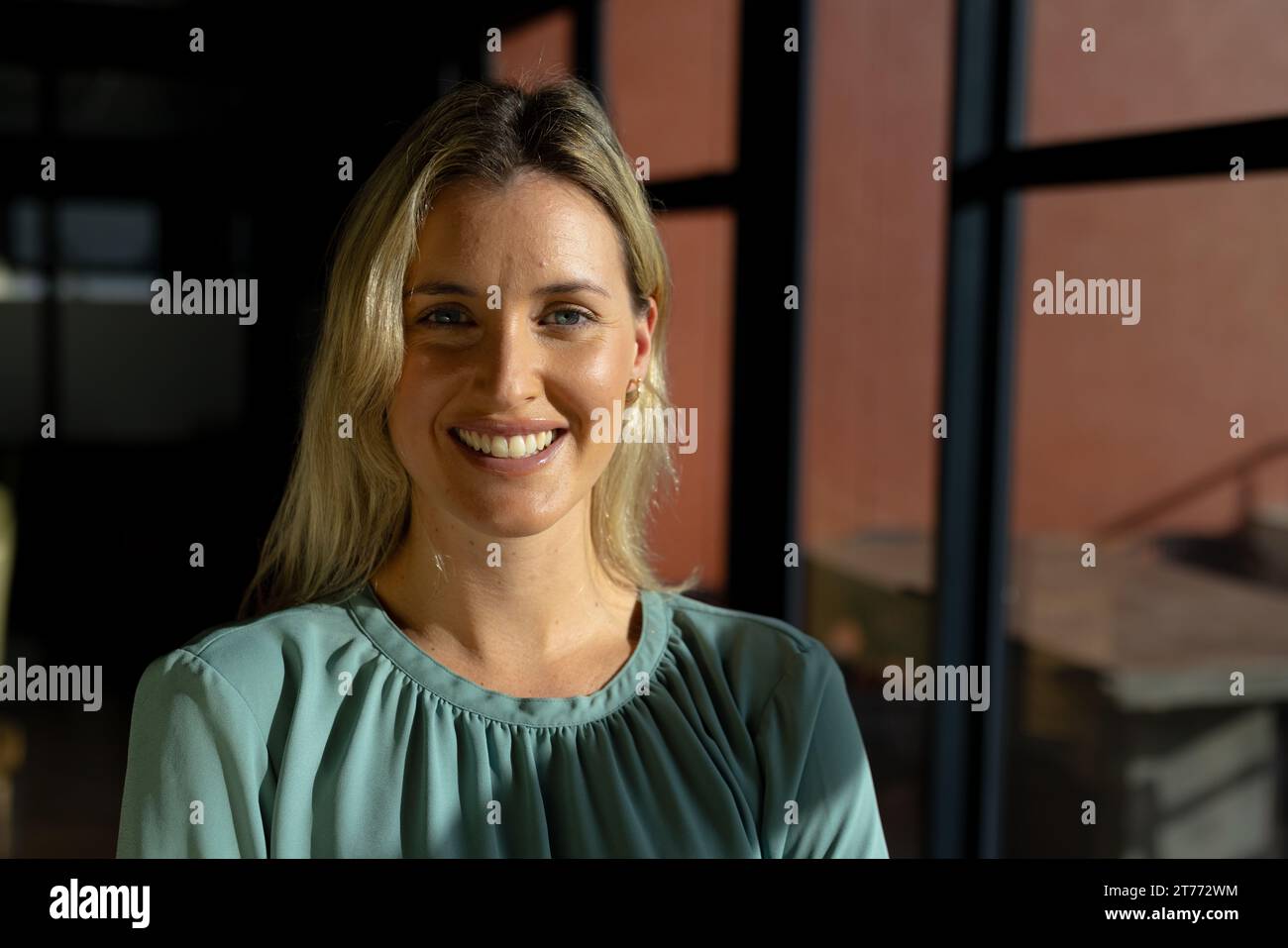 Portrait de blonde caucasienne femme d'affaires occasionnelle souriant au soleil au bureau, espace de copie Banque D'Images