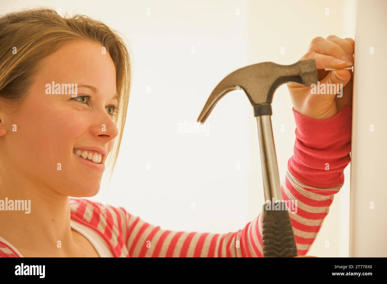 Femme martelant un clou dans un mur Banque D'Images