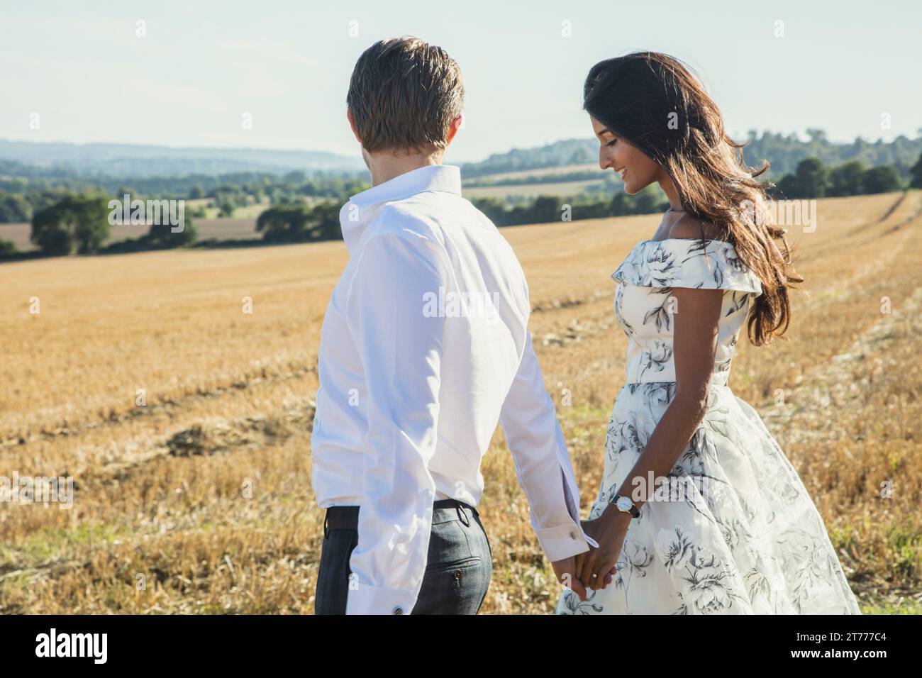 Couple en train de marcher dans un champ Holding Hands Banque D'Images