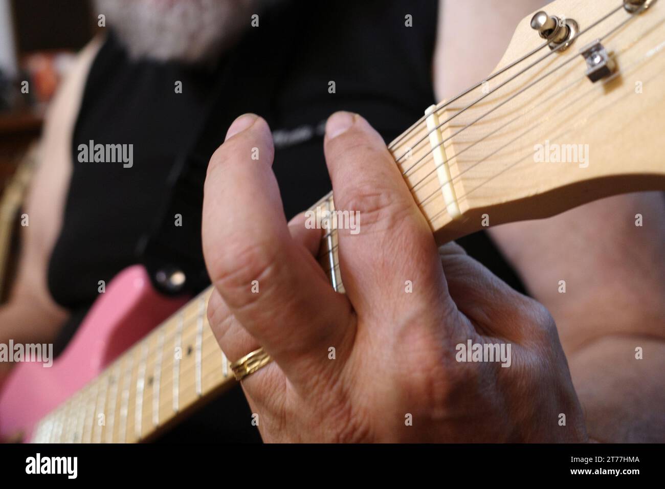 La main d'un homme qui joue un accord sur une guitare rose avec des cordes d'acier Banque D'Images