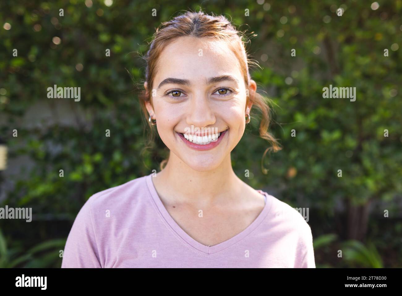 Portrait de femme biracial heureuse avec de longs cheveux bruns souriant dans le jardin ensoleillé Banque D'Images