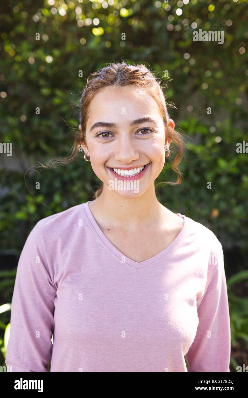 Portrait de femme biracial heureuse avec de longs cheveux bruns souriant dans le jardin ensoleillé Banque D'Images