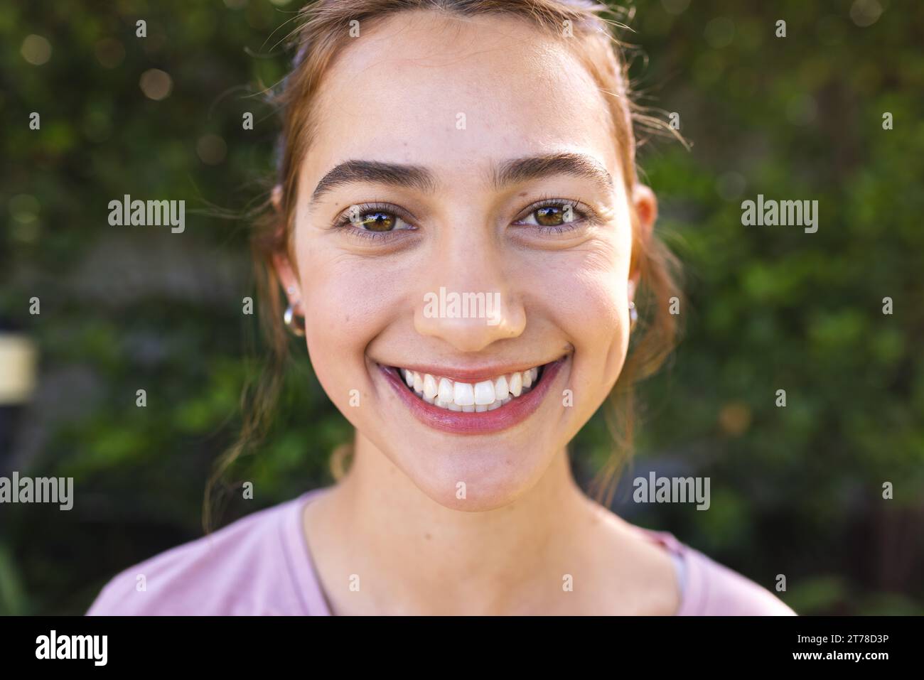 Portrait de femme biracial heureuse avec de longs cheveux bruns souriant dans le jardin ensoleillé Banque D'Images
