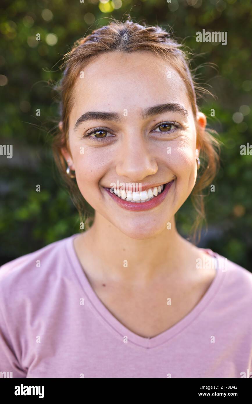 Portrait de femme biracial heureuse avec de longs cheveux bruns souriant dans le jardin ensoleillé Banque D'Images