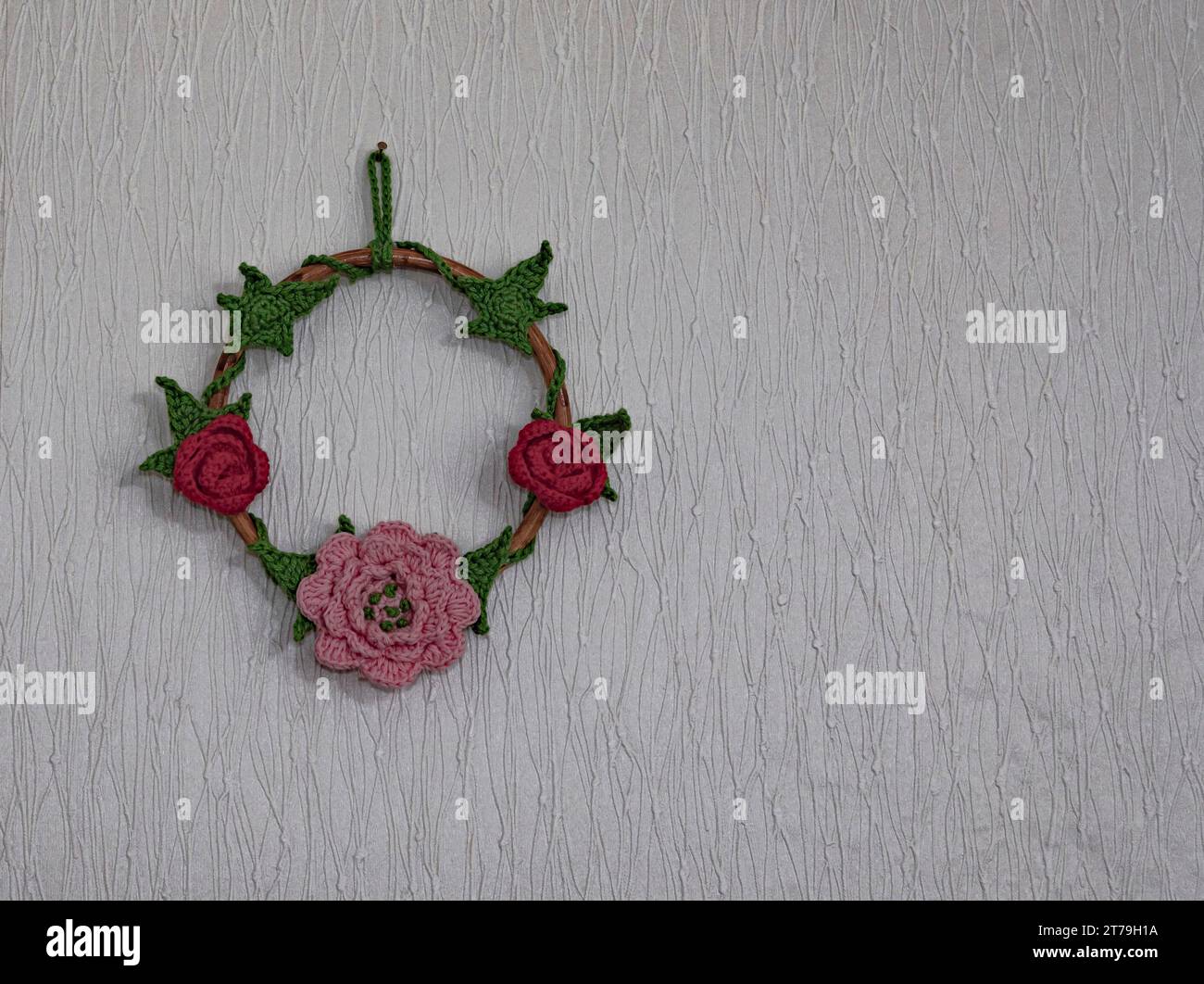 Bague en bois avec des fleurs au crochet et des feuilles en rouge, rose et vert sur fond blanc Banque D'Images
