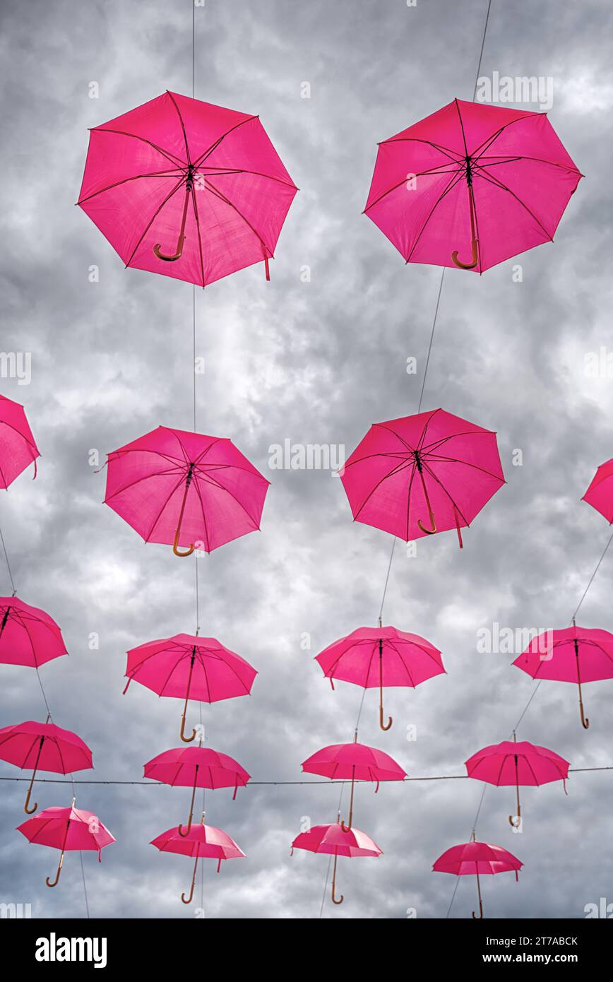 plusieurs parapluies ouverts roses suspendus dans le ciel avec un fond de nuage de humeur sombre Banque D'Images