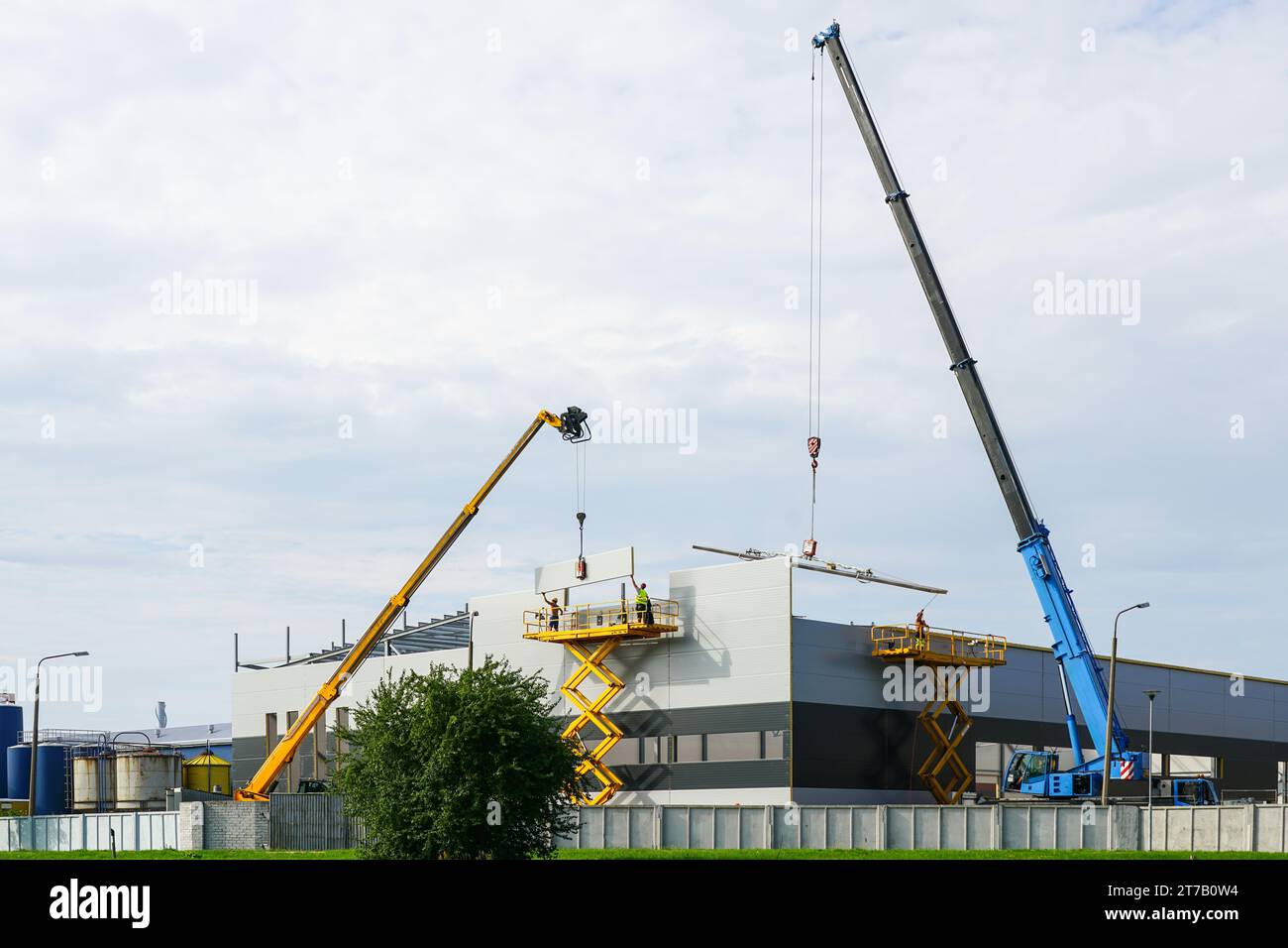 Assemblage des parois et du toit en panneaux sandwich à l'aide de deux grues à flèche télescopique et de deux élévateurs à ciseaux automoteurs Banque D'Images