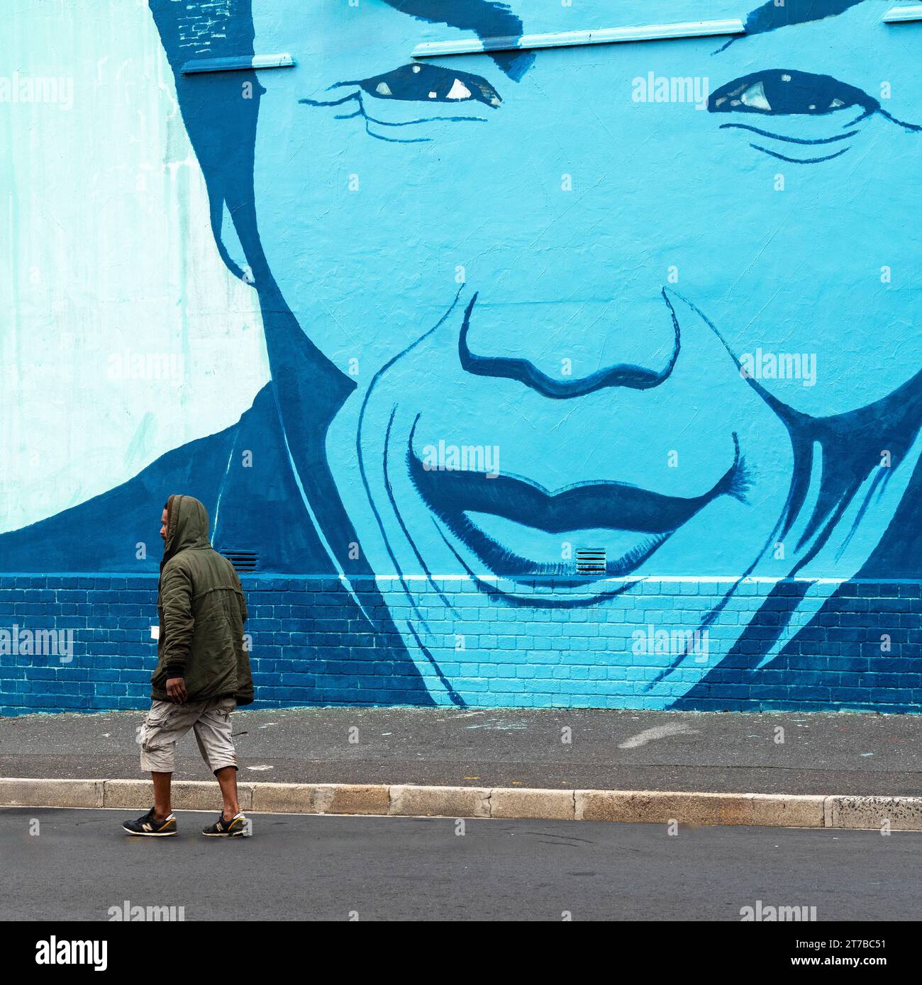 Un sans-abri marchant sur une route devant une peinture murale représentant Nelson Mandela. Banque D'Images