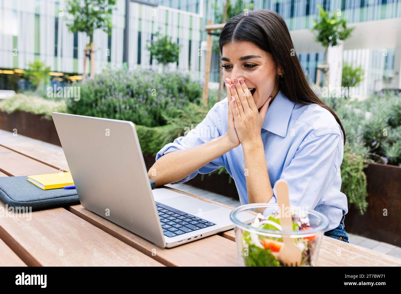 Femme d'affaires débordée de joie lisant un message inattendu sur un ordinateur portable à l'extérieur. Banque D'Images