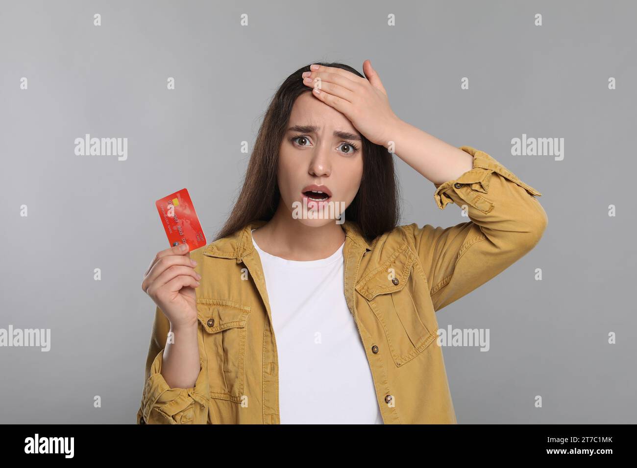 Femme choquée avec carte de crédit sur fond gris clair. Problème de dette Banque D'Images