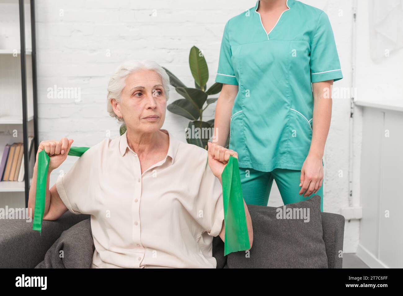 Femme âgée s'exerçant avec la bande élastique verte assise à l'avant infirmière féminine Banque D'Images
