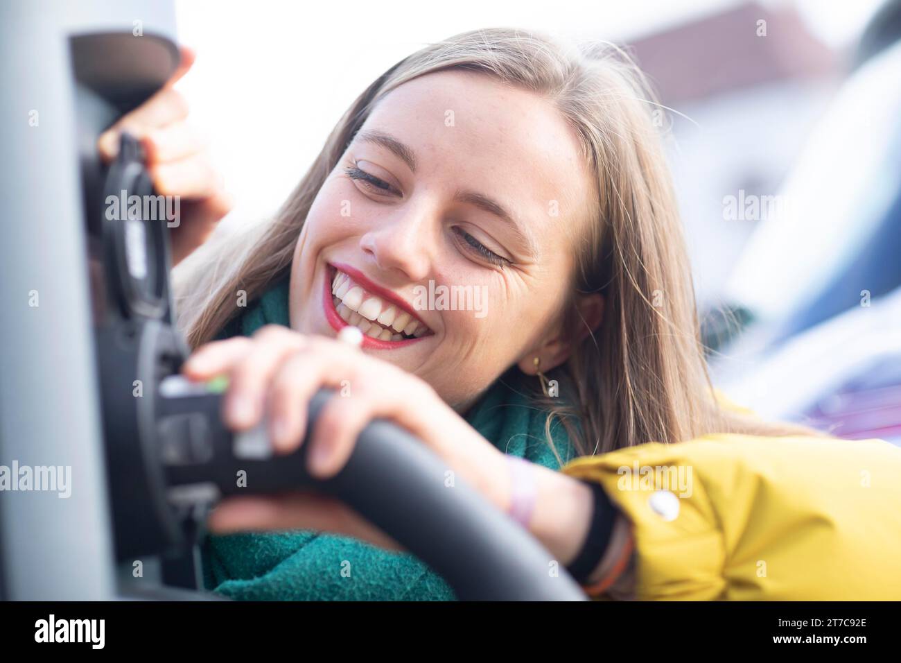 Jeune femme avec câble de recharge à une station e-car Banque D'Images