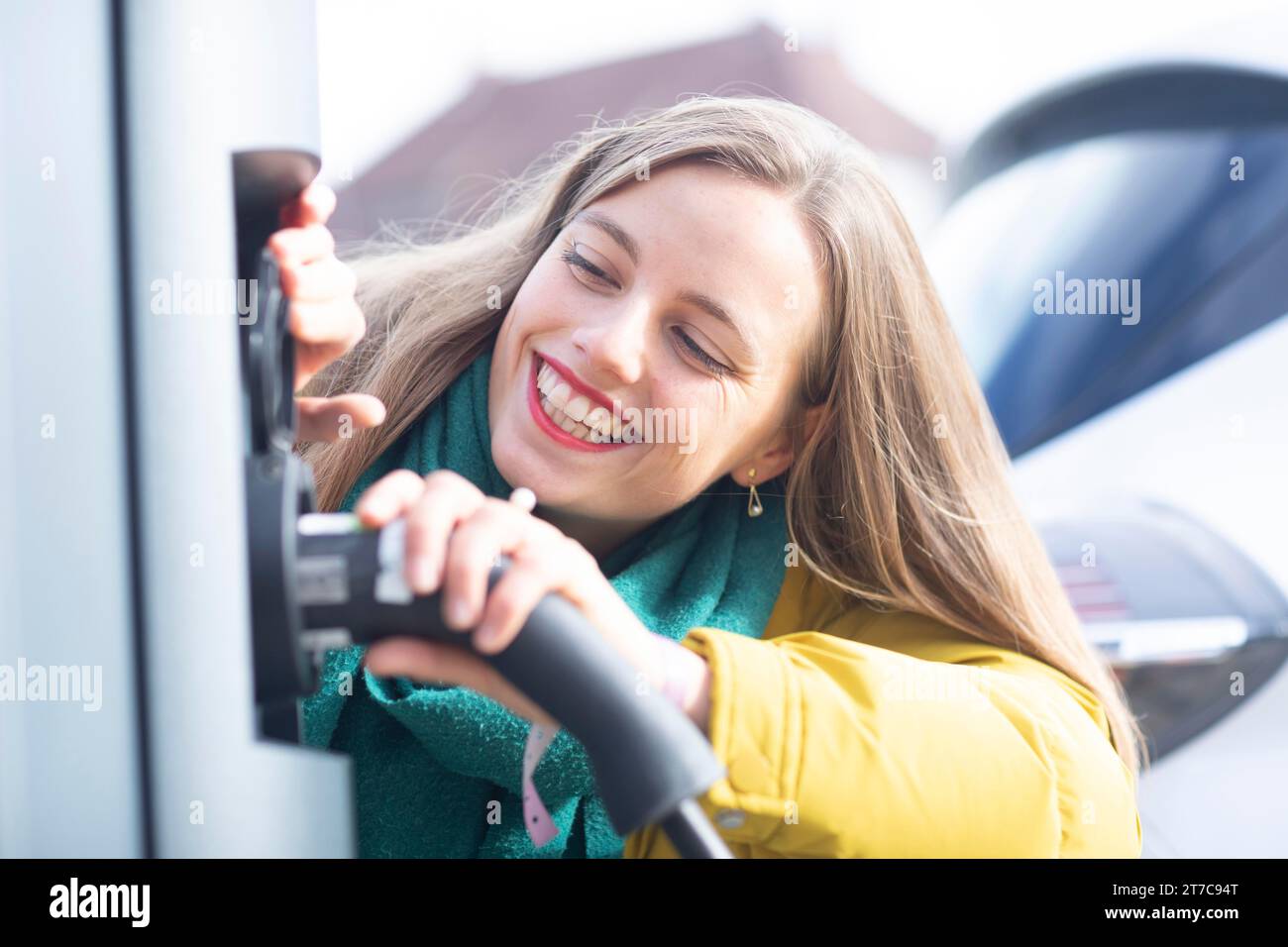 Jeune femme charge avec câble de recharge pour voiture électrique dans la ville Banque D'Images