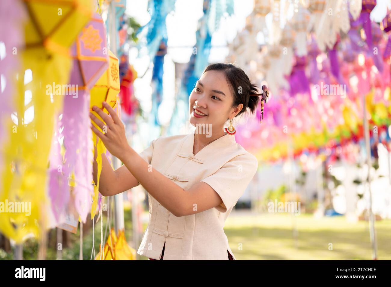 Une belle et heureuse femme thaï-asiatique en robe traditionnelle accroche une lanterne en papier et profite du festival YI Peng ou Loy Krathong dans un temple de CH Banque D'Images