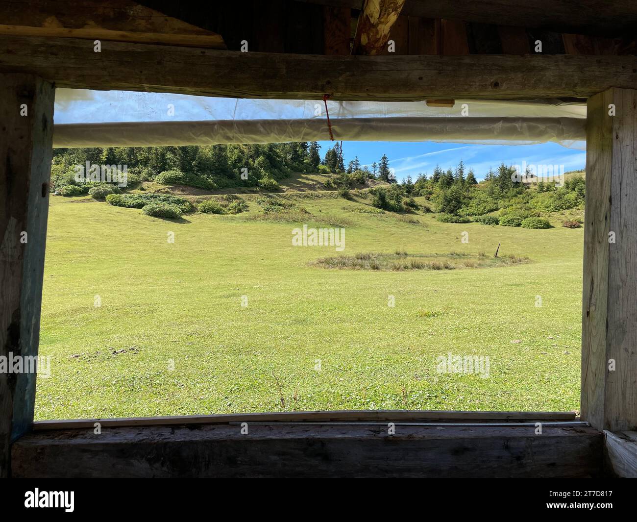 Une vue panoramique d'une fenêtre de cabine en bois donnant sur un paysage rural verdoyant par une journée ensoleillée Banque D'Images