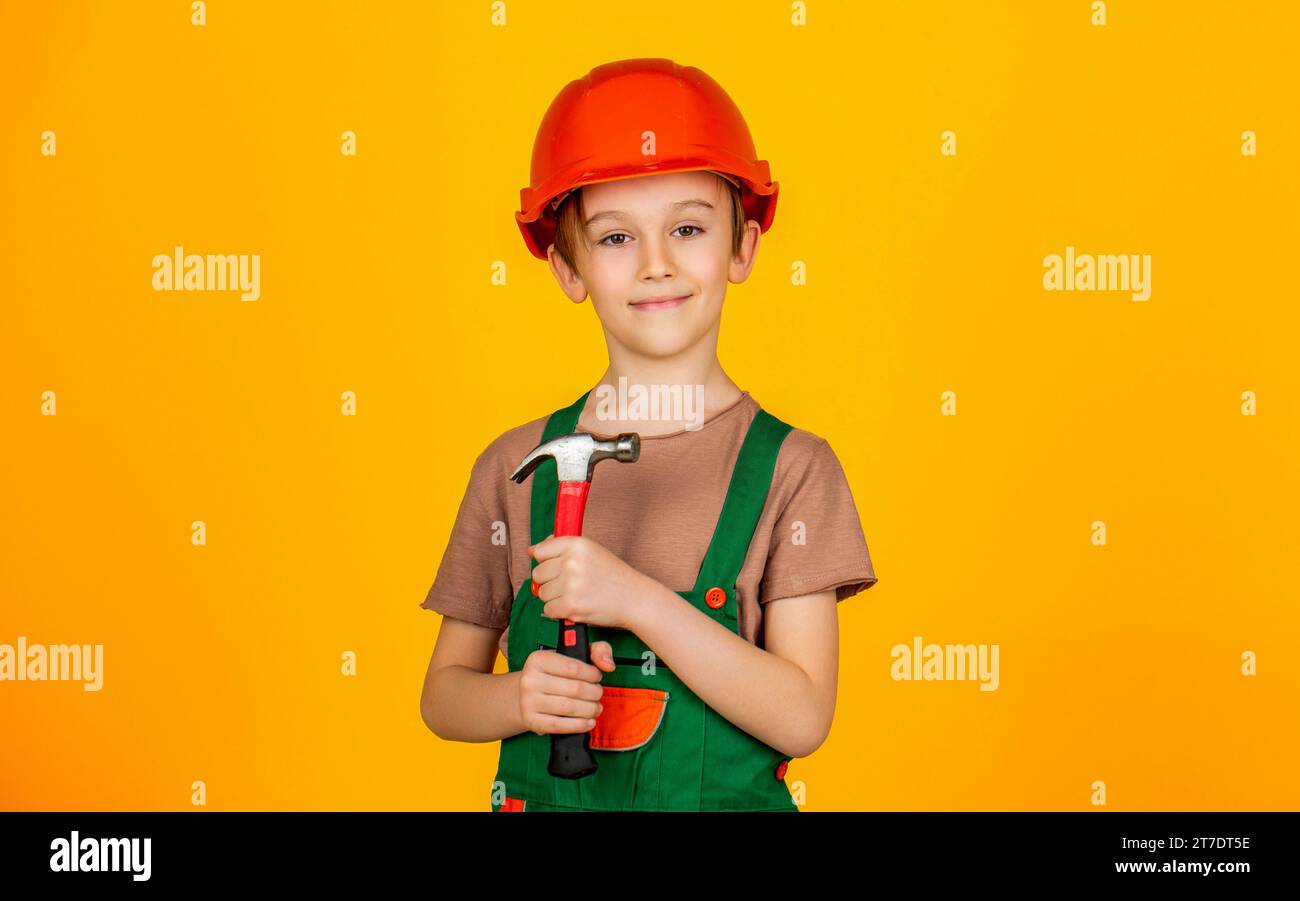 Petit constructeur dans le marteau de hardhats. Casque de construction pour enfants, casque de sécurité. Martelage par marteau. Petit constructeur en casque et hummer. Enfant habillé en ouvrier Banque D'Images