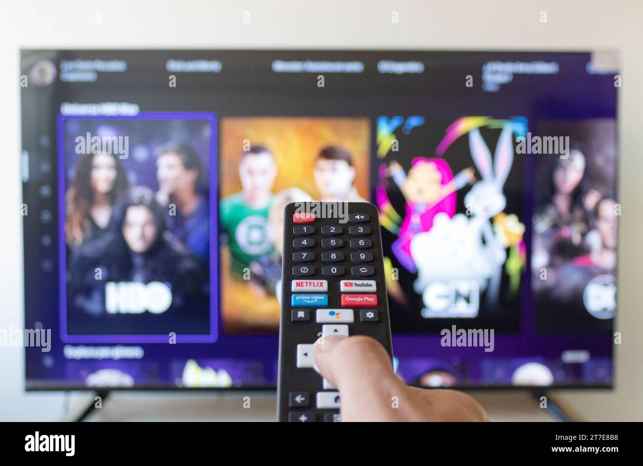 Gros plan sur un homme de la main droite tenant une télécommande de télévision intelligente noire recherchant dans l'application HBO MAX en streaming Banque D'Images