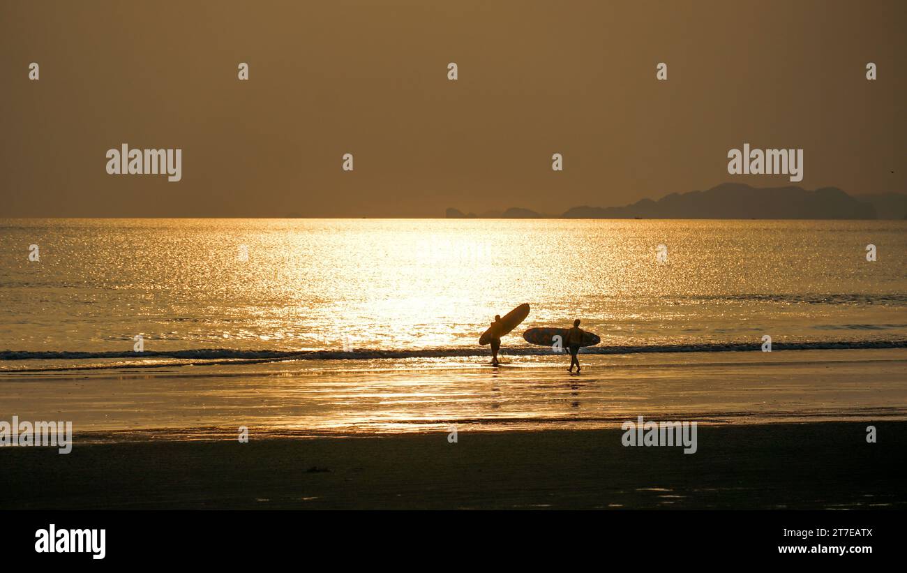 Silhouette de surfeur deux hommes portant leur planche de surf sur la plage de coucher du soleil, mode de vie santé et sport. Banque D'Images