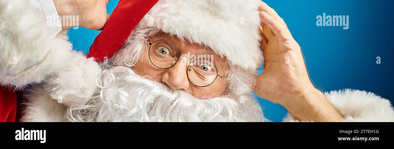 Portrait du Père Noël excité avec barbe blanche et lunettes regardant la caméra sur bleu, bannière Banque D'Images