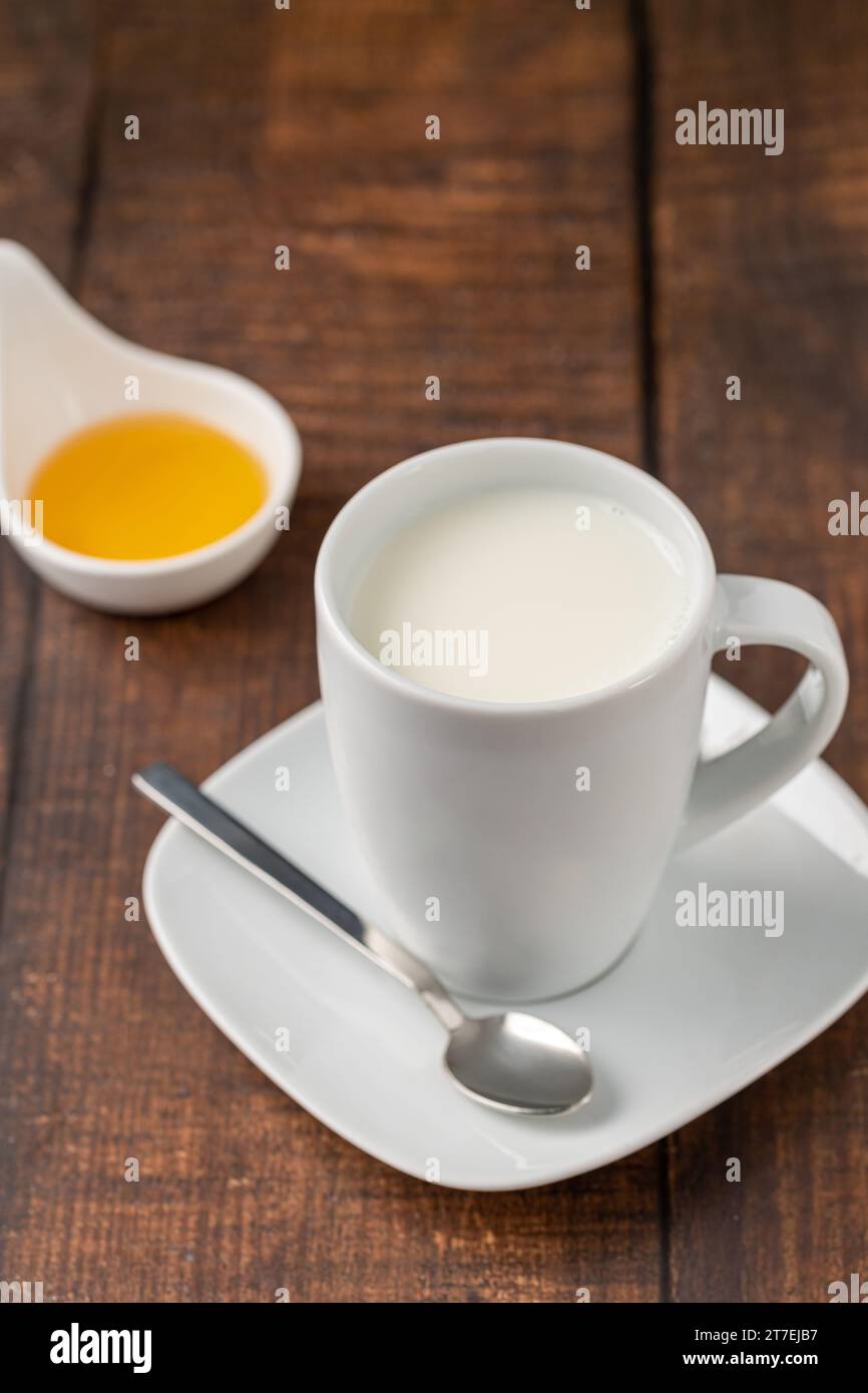 Lait dans une tasse en porcelaine et miel dans un bol en porcelaine sur une table en bois Banque D'Images