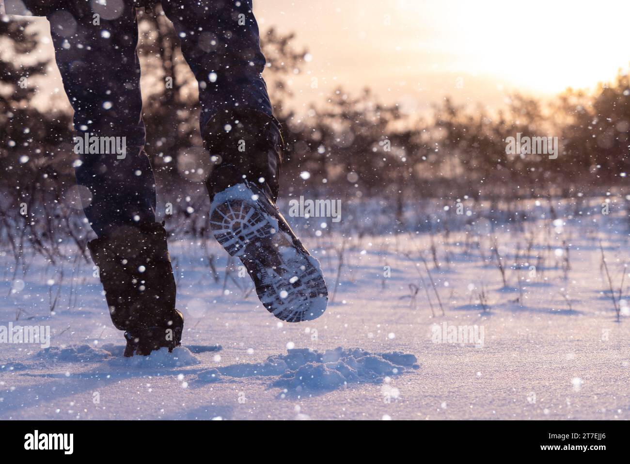 Un voyageur en bottes marche le long d'une route hivernale enneigée. Banque D'Images